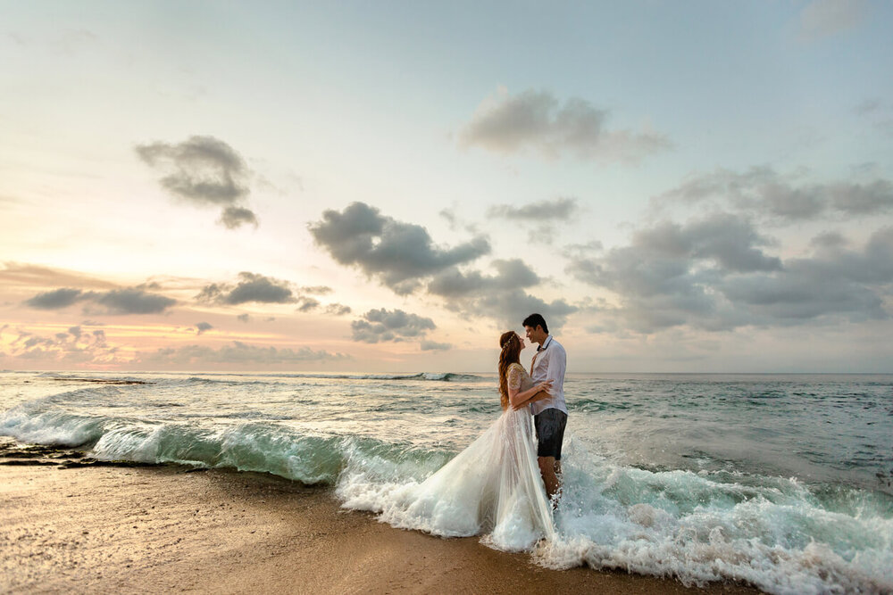 landscape photograph of bride and groom embracing on beach with waves.jpg
